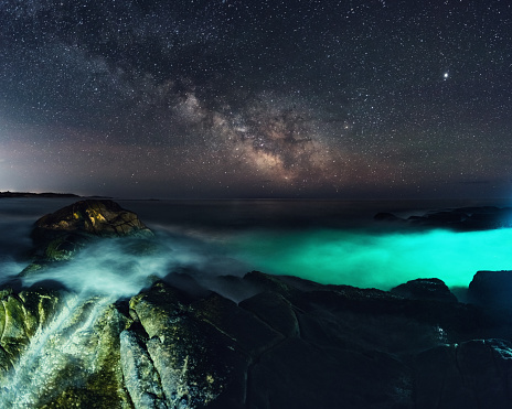 The Summer Milky Way arcs high above an illuminated cove on the Atlantic coast of Nova Scotia.  Long exposure.