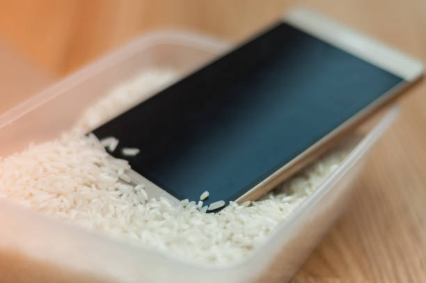 agua teléfono dañado en una caja de arroz - ahogar fotografías e imágenes de stock