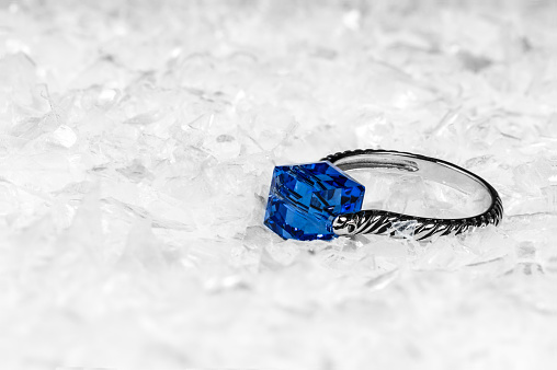Engagement ring with blue diamond/crystal on white snow background.