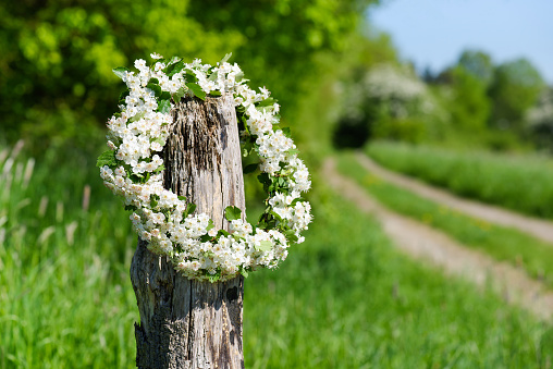 Wreath from spring flowers of the hawthorn hanging on an old wood fence post against the background of village road.