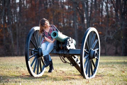 Young woman sitting on old cannon looking inside in Manassas National Battlefield Park in Virginia where Bull Run battle was fought