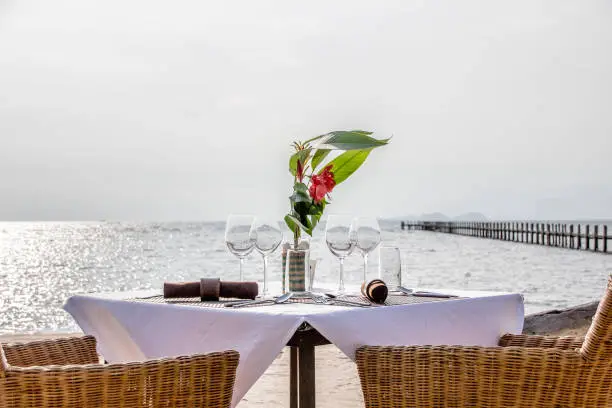 A table set with wine glasses and flowers for a private dinner by the beach with an ocean view.