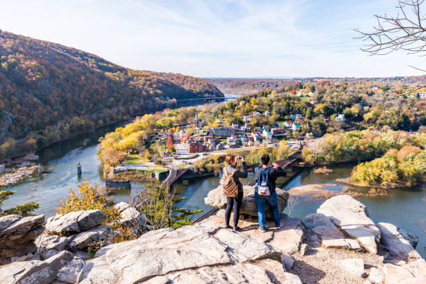Overlook with hiker people women couple, colorful orange yellow foliage fall autumn forest with small village town by river in West Virginia, WV Harper's Ferry, USA - November 11, 2017: Overlook with hiker people women couple, colorful orange yellow foliage fall autumn forest with small village town by river in West Virginia, WV harpers ferry photos stock pictures, royalty-free photos & images
