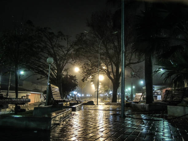 A public square during light rain at night, with wooden banks covered by raindrops, in the rural city of Nova Resende, in Minas Gerais state, Brazil.