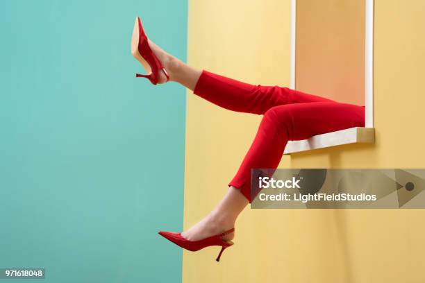 Pandangan Parsial Wanita Dengan Celana Merah Dan Sepatu Outstretching Kaki Keluar Jendela Dekoratif Foto Stok - Unduh Gambar Sekarang