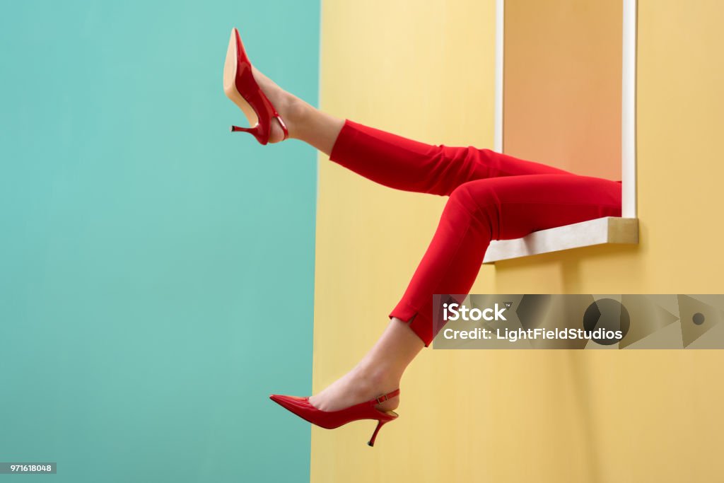 partial view of woman in red pants and shoes outstretching legs out decorative window Fashion Stock Photo