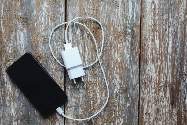 istock White charger and black smartphone on old wooden background. Information technology horizontal digital photo. Modern layout on vintage texture. 971636224