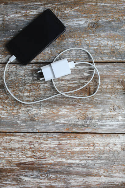 istock White charger and black smartphone on old wooden background. Information technology vertical digital photo. Modern layout on vintage texture. 971636246