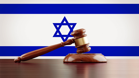 Wooden gavel in front of Israeli flag. The gavel is nicely textured and it is casting soft shadows on the ground. Great use for law, justice and auction related concepts.