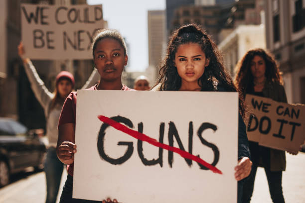 Say no to guns Two girls holding a banner with word guns strikethrough. Women holding sign that says not guns at a rally. gun stock pictures, royalty-free photos & images