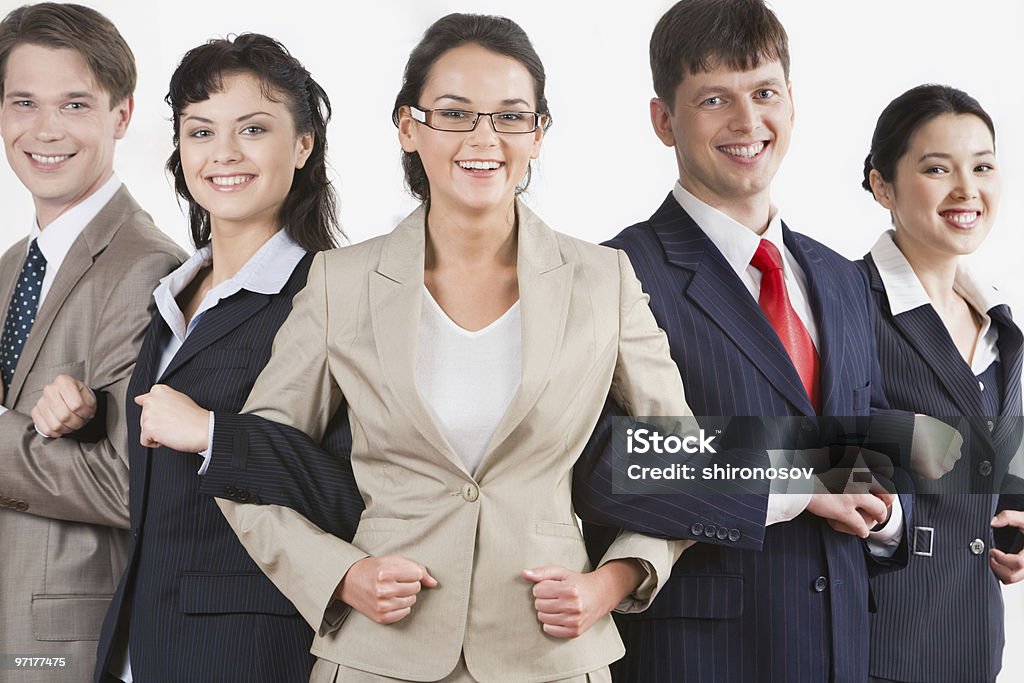 Businesspeople linking arms symbolizing alliance Photo of five business partners holding each other by arms making chain and looking at camera Adult Stock Photo