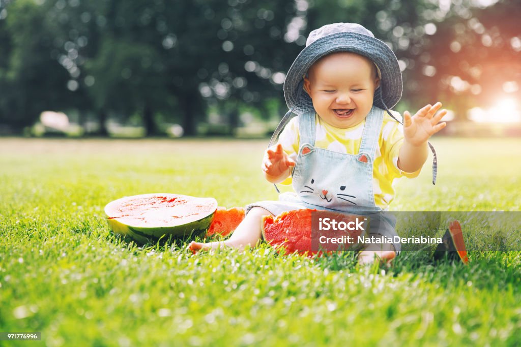 Más lindo sonriente niña comiendo sandía sobre hierba verde durante el verano. - Foto de stock de Bebé libre de derechos
