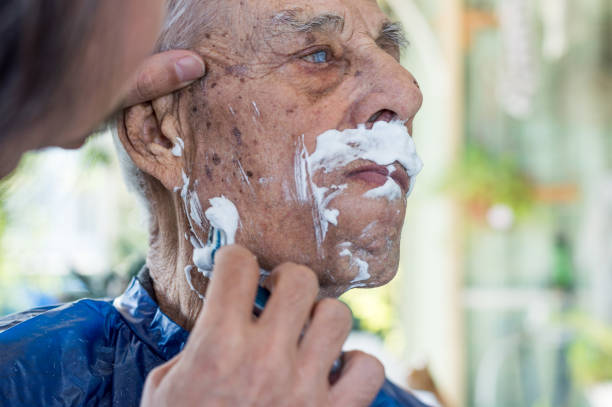 Old man getting his beard shaved by young skilled man at home stock photo