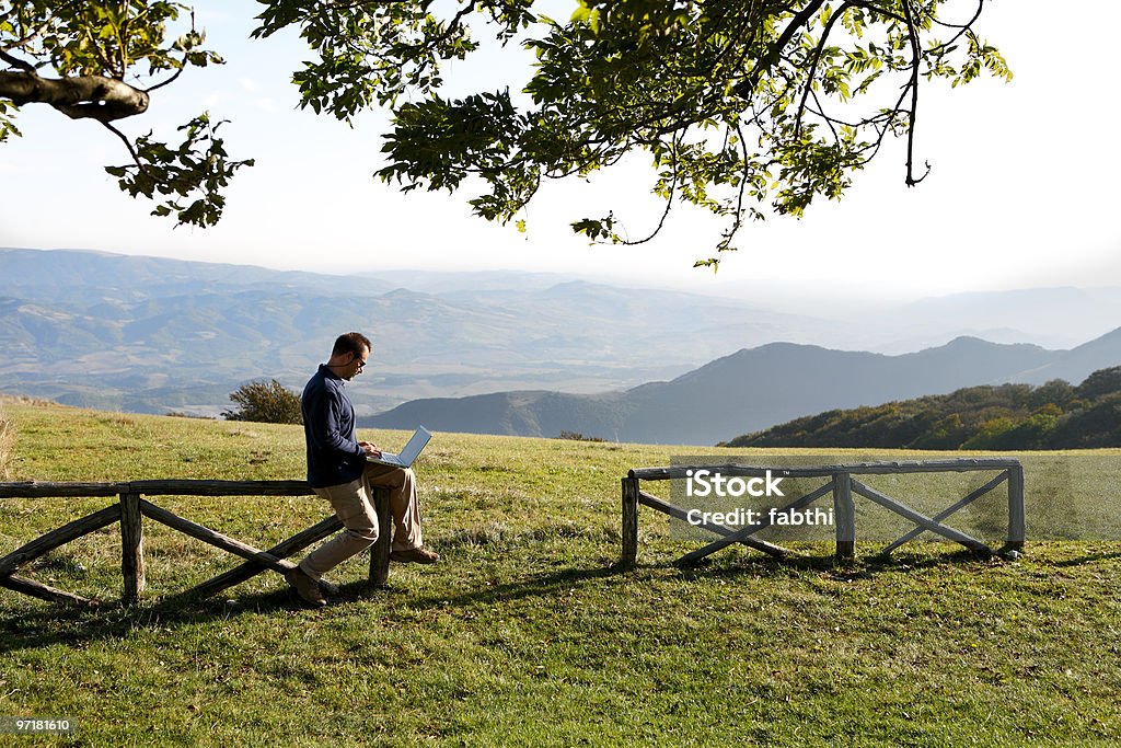 Человек, сидящий на забор в сельской местности с помощью ноутбука - Стоковые фото 30-34 года роялти-фри