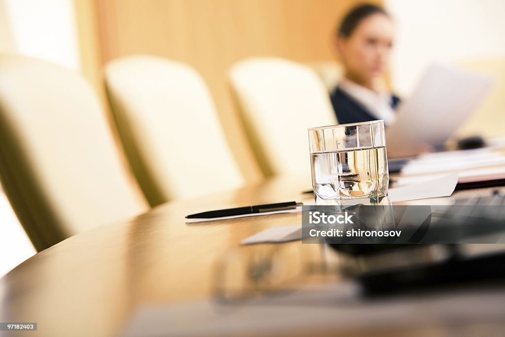 Close up of a glass of water on a conference table Close-up of glass of water on the background of chairs, papers and working woman Arranging Stock Photo