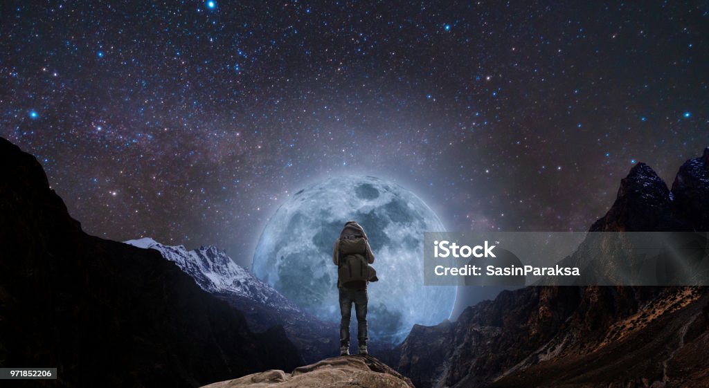 un hombre con la situación de la mochila en el pico de la montaña en la noche y montaña de silueta con luna llena brillante y un cielo lleno de estrellas - Foto de stock de Soñar despierto libre de derechos