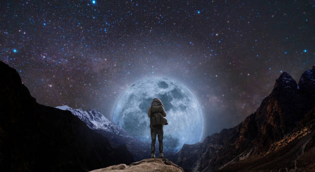 istock a man with backpack standing on mountain peak at night, and silhouette mountain with bright full moon and sky full of stars 971852206