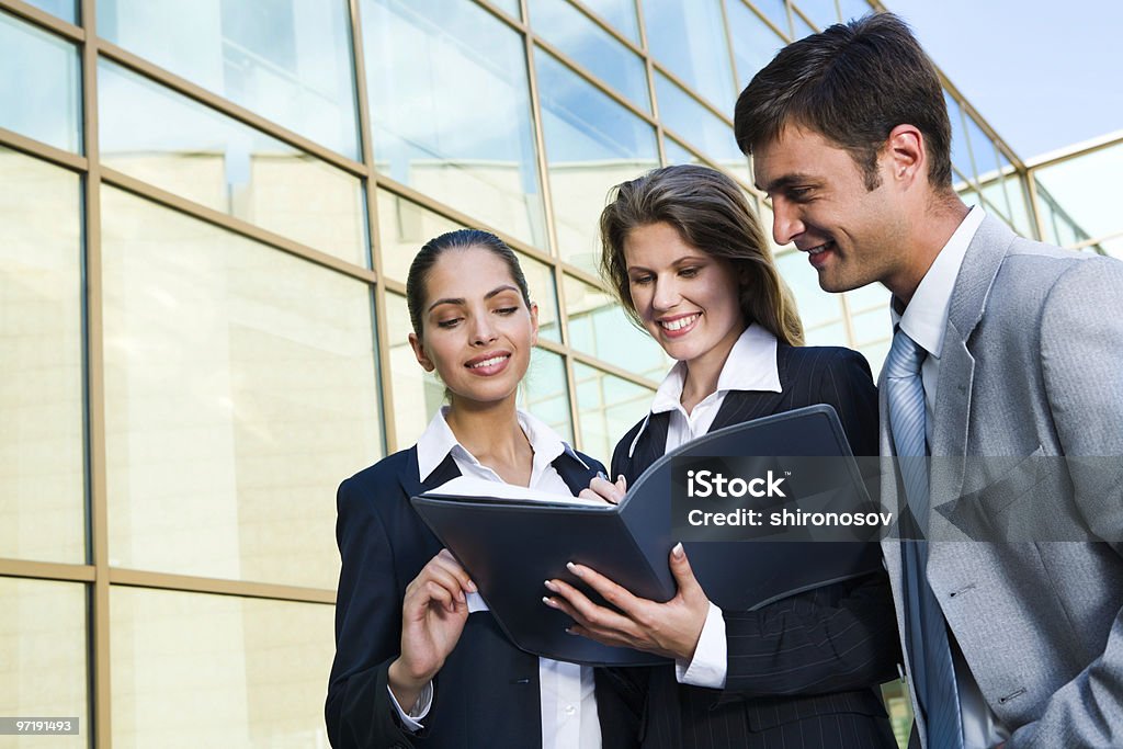 Three business people reviewing a business agreement The business women signs the agreement with her partners on a background of a building Adult Stock Photo