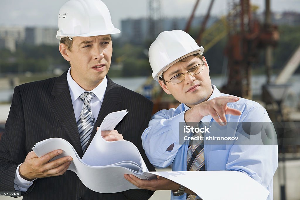 Two businessmen in hard hats, holding plans, meet onsite Director is showing a place of construction to the architect Adult Stock Photo