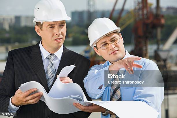 Two Businessmen In Hard Hats Holding Plans Meet Onsite Stock Photo - Download Image Now