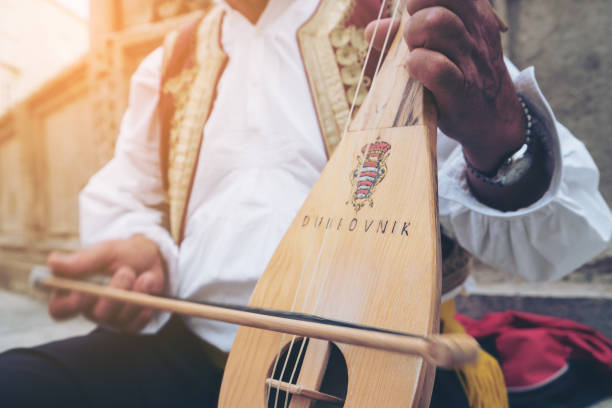 Man Plays Croatian Musical Instrument in Dubrovnik A busker plays traditional Croatian folk music with a 3-string instrument (lijerica) in the old city of Dubrovnik, Croatia. dubrovnik stock pictures, royalty-free photos & images