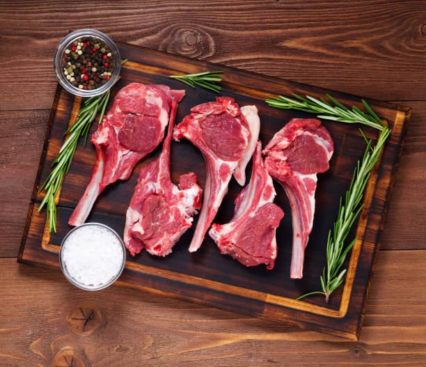 istock Raw lamb cutlets on bone on dark brown wooden background, lamb ribs, top view. 971961224