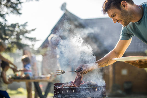 glücklicher mann grillen von fleisch auf einem grill im freien. - grill zubereitung stock-fotos und bilder