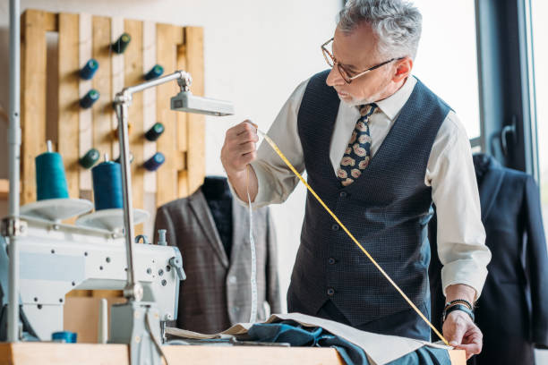 istock grey hair tailor measuring cloth with tape measure at sewing workshop 972009672