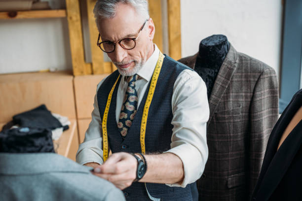 istock handsome mature tailor with measuring tape looking at jacket on mannequin at sewing workshop 972009746