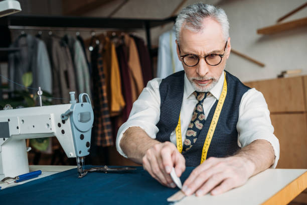 istock senior tailor drawing outline on cloth at sewing workshop 972009912