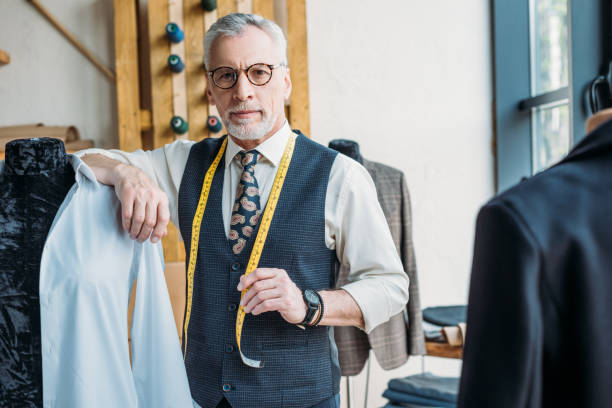 istock handsome tailor leaning on mannequin at sewing workshop and looking at camera 972009944