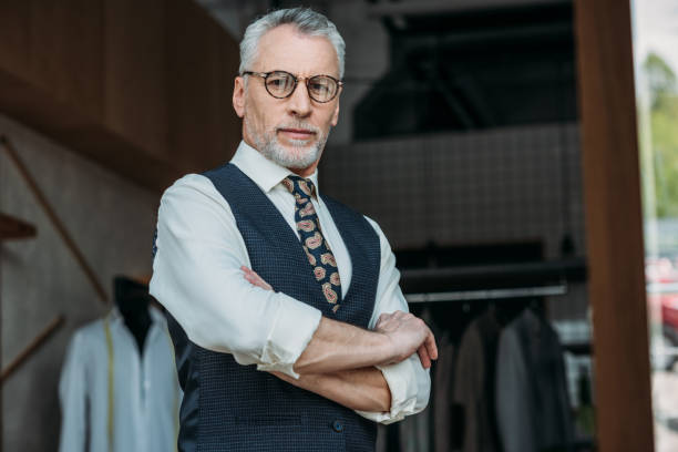 istock handsome senior tailor standing with crossed arms and looking at camera at sewing workshop 972010040