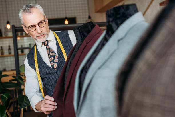 istock focused mature tailor with measuring tape and notebook  examining jackets on mannequins at sewing workshop 972011262