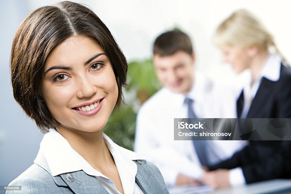 A smiling woman with two business people talking behind her Face of beautiful woman on the background of business people Business Stock Photo