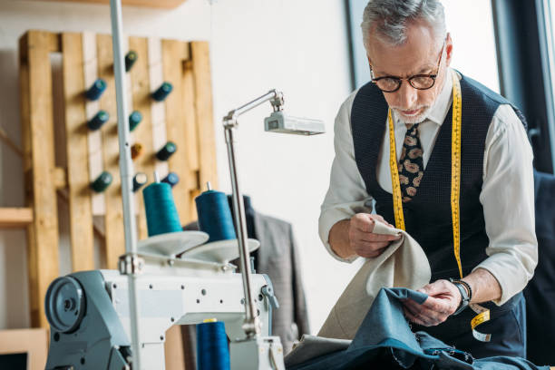 handsome tailor choosing between dark and light clothes at sewing workshop handsome tailor choosing between dark and light clothes at sewing workshop tailor photos stock pictures, royalty-free photos & images