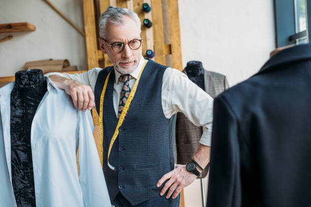 istock handsome tailor leaning on mannequin at sewing workshop and looking at jacket 972013720