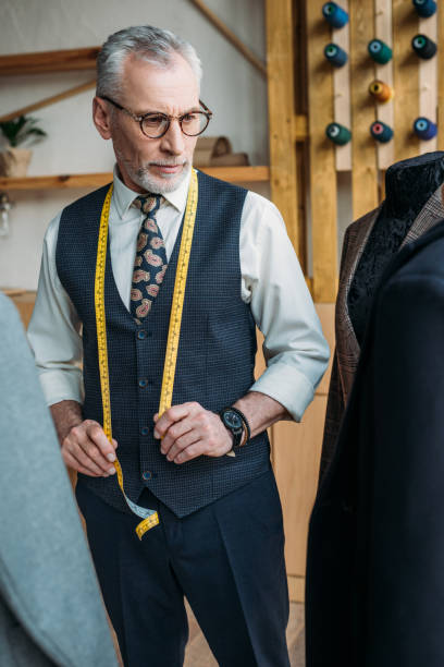 istock handsome tailor looking at jackets on mannequins at sewing workshop 972016294