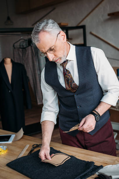 istock serious mature tailor looking at paper pockets pattern to postpone it on cloth at sewing workshop 972029474