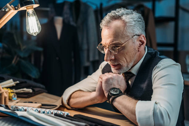 istock confident mature tailor looking at cloth samples at sewing workshop in late evening 972033028