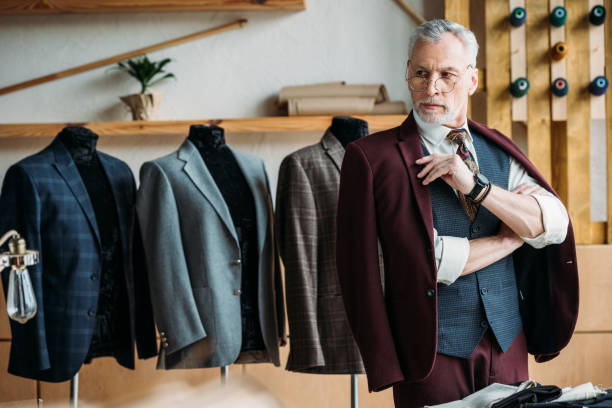 istock serious mature tailor in stylish clothes at sewing workshop 972033176