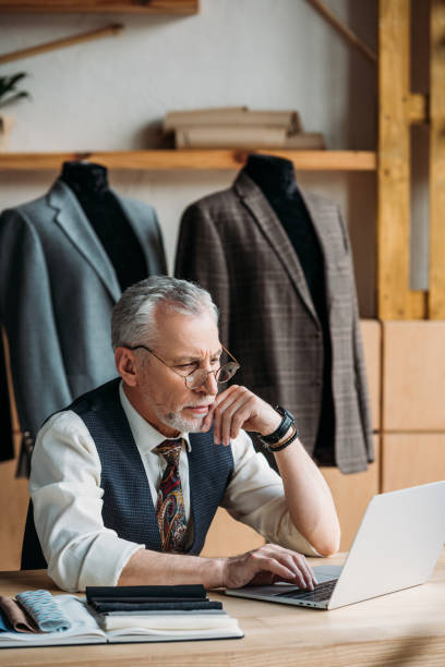 istock concentrated mature tailor working with laptop at sewing workshop 972035848