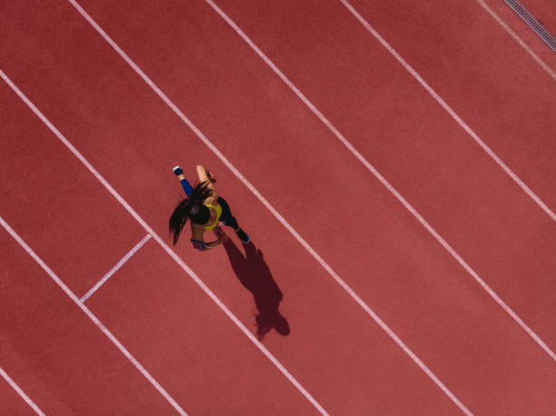 Female runner listening to music and running on sports track Young female professional athlete listening to music and training by sprinting on running track lane marker stock pictures, royalty-free photos & images