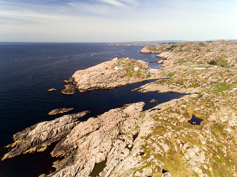 Photo of Lindesnes beacon in summer, South Norway. Aerial shot. Rocky sea coast and blue sky. Red and white lighthouse.