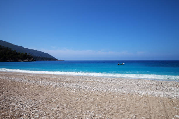 Sand beach with pebble stones and beautiful blue sea Sand beach with pebble stones and beautiful blue sea at warm sunny summer day. Mediterranean sea, Turkey. cusp stock pictures, royalty-free photos & images