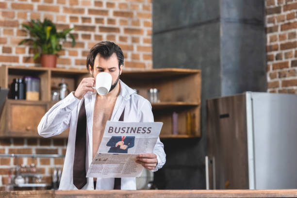 istock handsome loner businessman drinking coffee and reading newspaper at kitchen 972063692