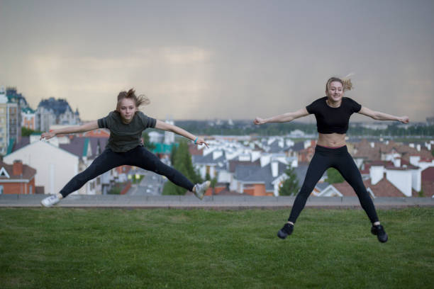 istock Two young female gymnasts doing acrobatics jumps with cityscape on background 972063770