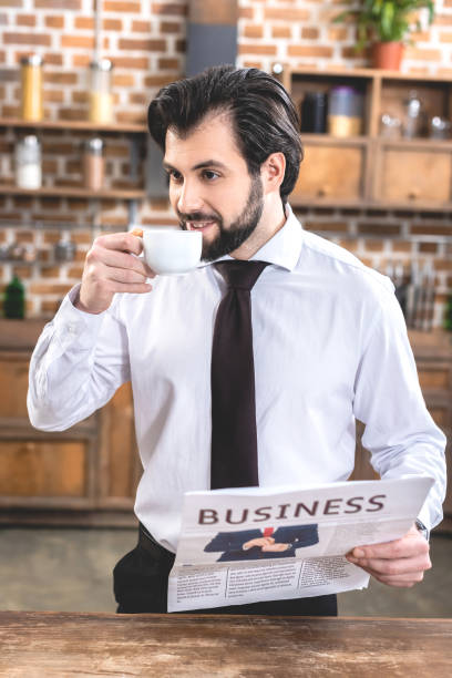 istock handsome loner businessman drinking coffee and holding newspaper at kitchen 972064458