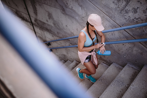 Sporty woman working out by running up urban stairs and monitoring heart rate on smartwatch