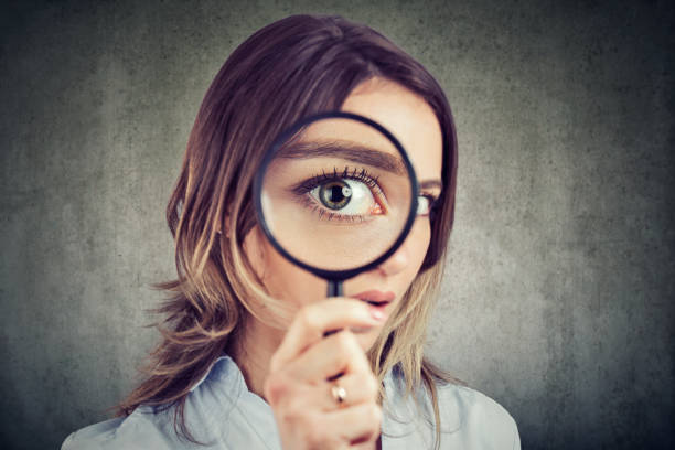 curious woman looking through a magnifying glass - obsessive imagens e fotografias de stock