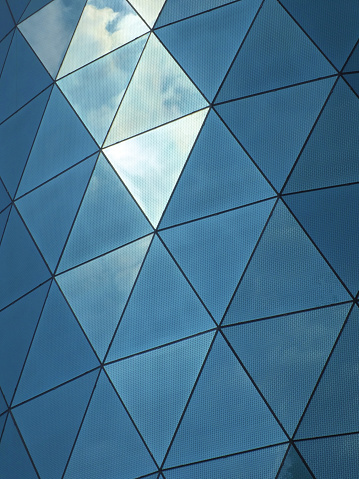 close up of a modern corporate building with angular patterned mirrored windows panes reflecting the sky and clouds